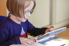 Mädchen betrachtet Buchseite mit Hilfe einer elektronischen Lupe