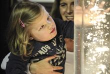 Frühförderin und Kind spielen mit der Blubbersäule – einer leuchtenden und vibrierenden Wassersäule mit Luftblasen
